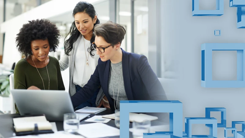 A group of business women look at something on a laptop screen in an office