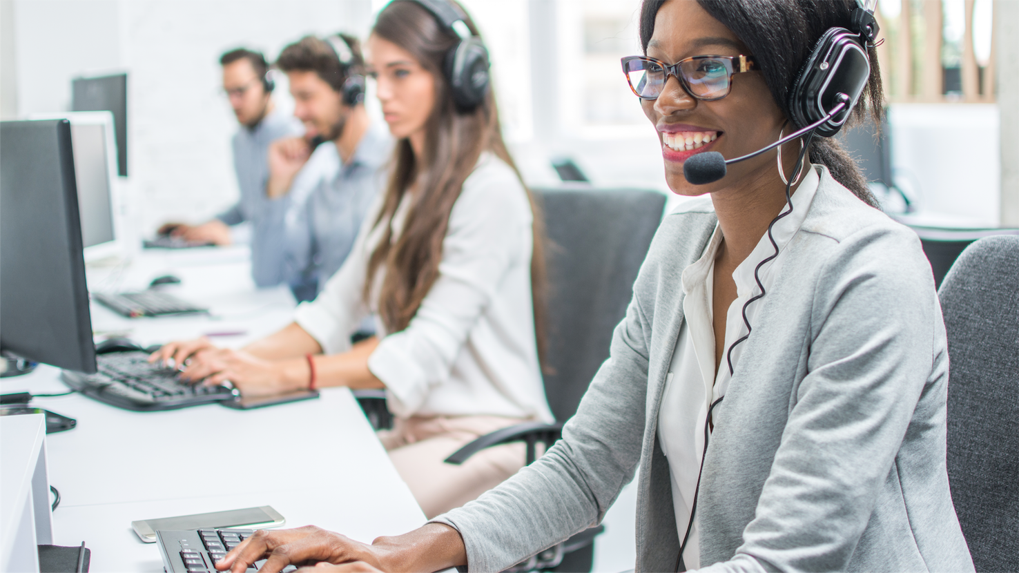 Customer service agents sitting with headsets at laptops smiling