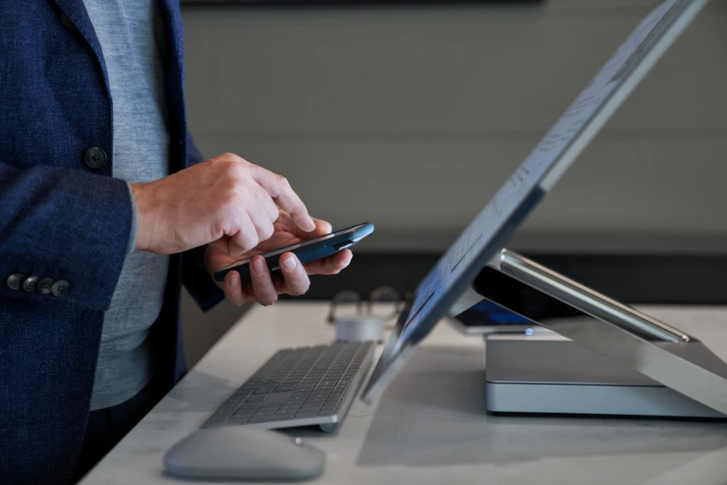 Multi-factor authentication prevents 99.9% of credential attack, helping your security. A man types in a code on his phone at his work station.