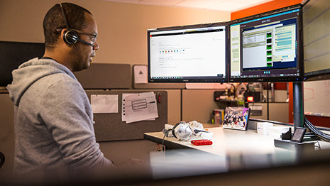 Image of a firstline worker speaking to a colleague over a headset while looking at several computer monitors