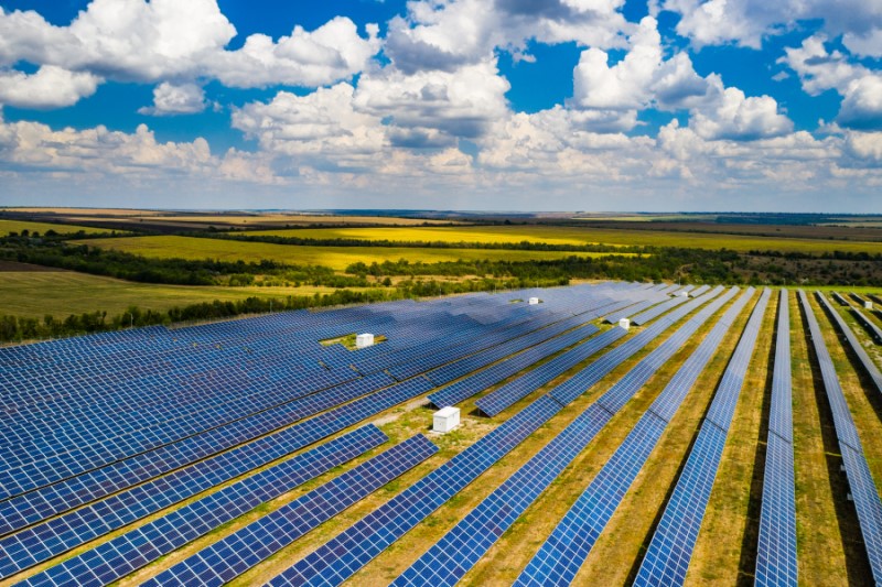 An expansive solar array stretches across fields, under a bright sky