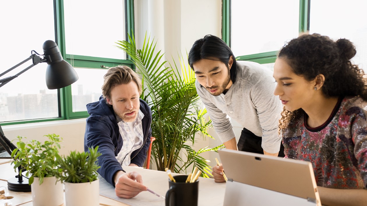 A group of people sitting at a table collaborating on work and using a laptop computer