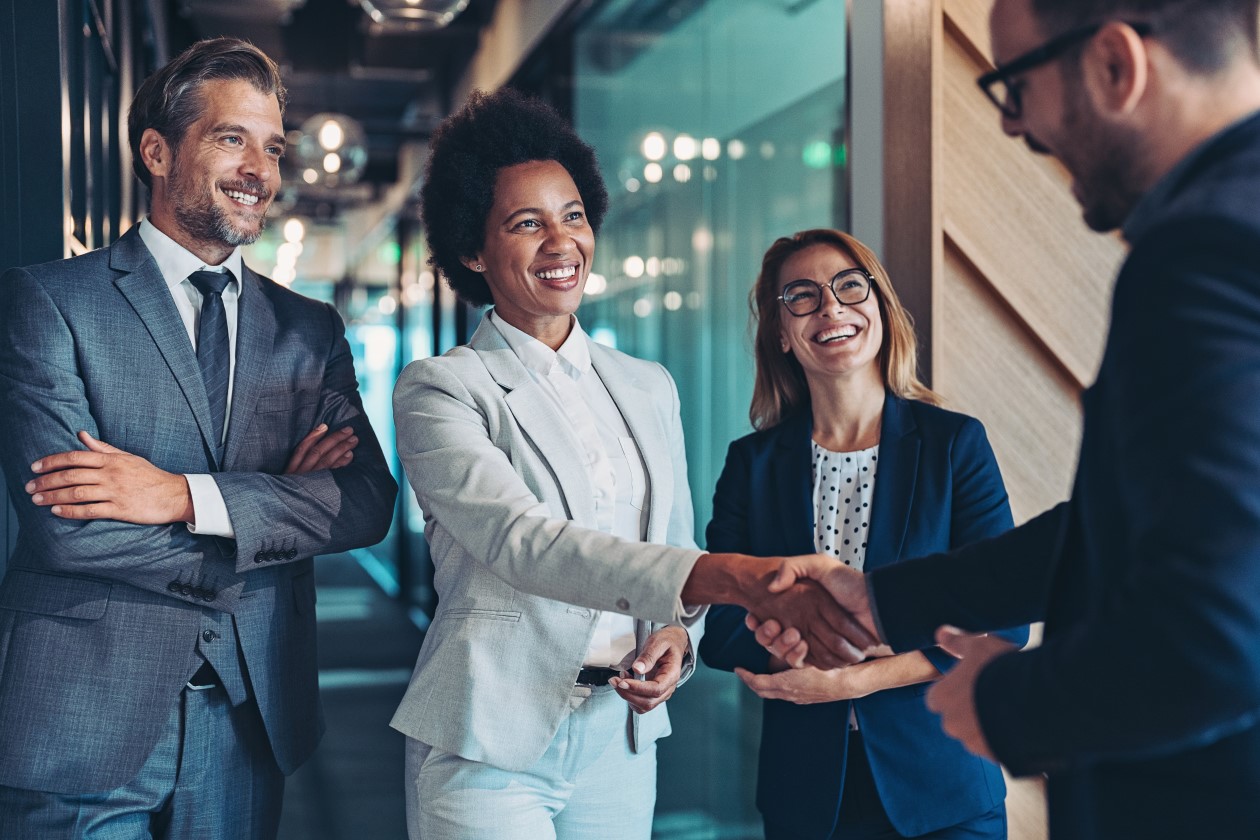 Four business people smiling, two of which shaking hands