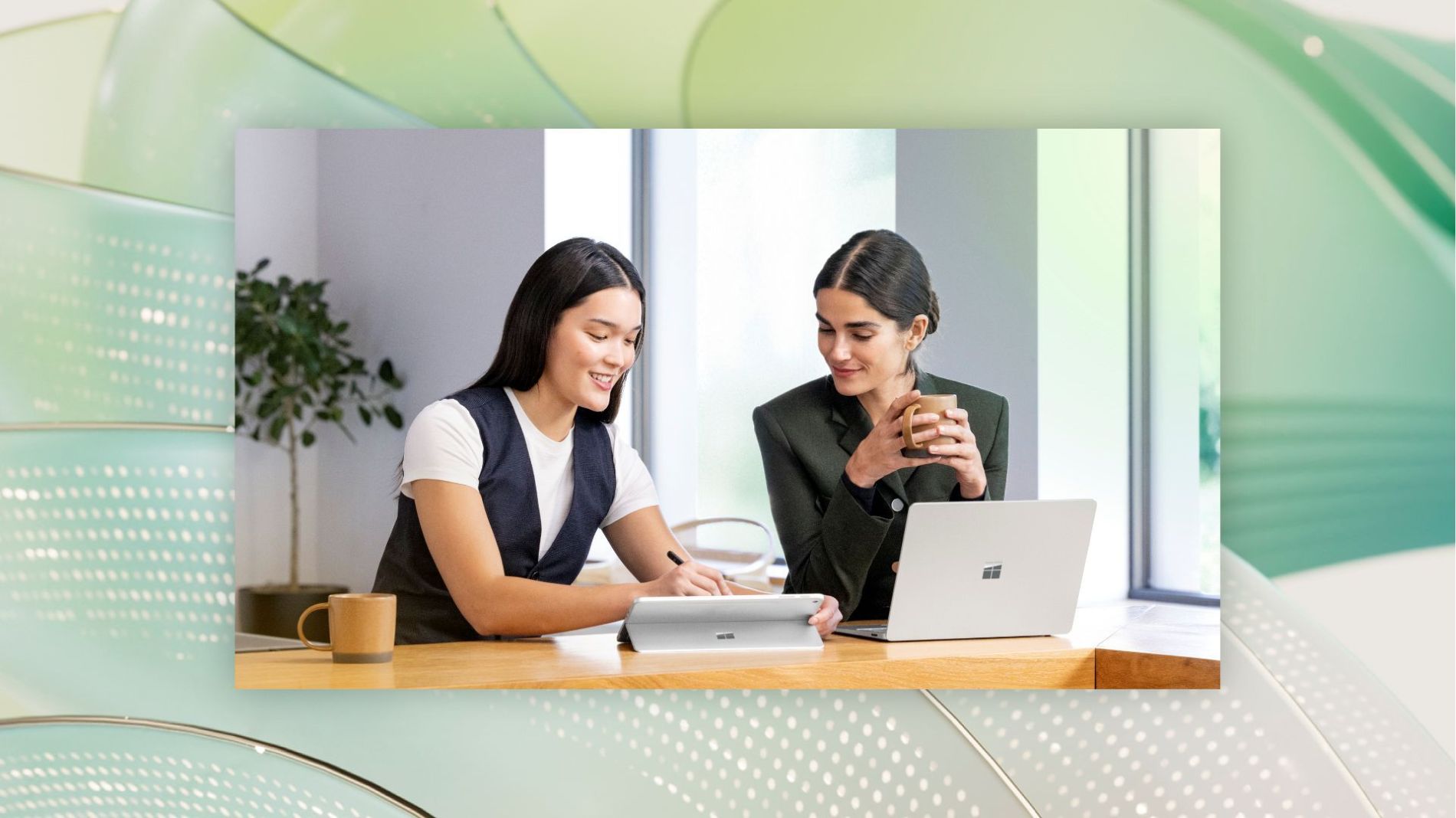 Two professionals collaborate at a desk using a Microsoft Surface laptop and tablet, reviewing digital information together in a modern office setting
