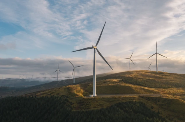 Wind turbines on rolling hills at sunrise, generating renewable energy above a forested landscape