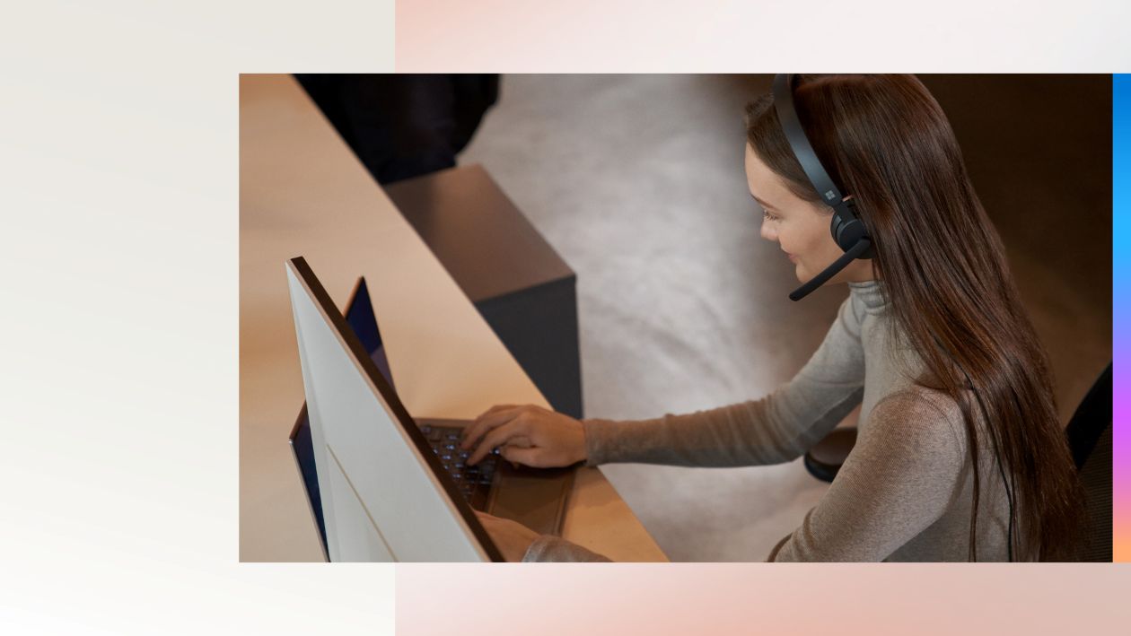 A person working on a computer while wearing a headset with a mouthpiece