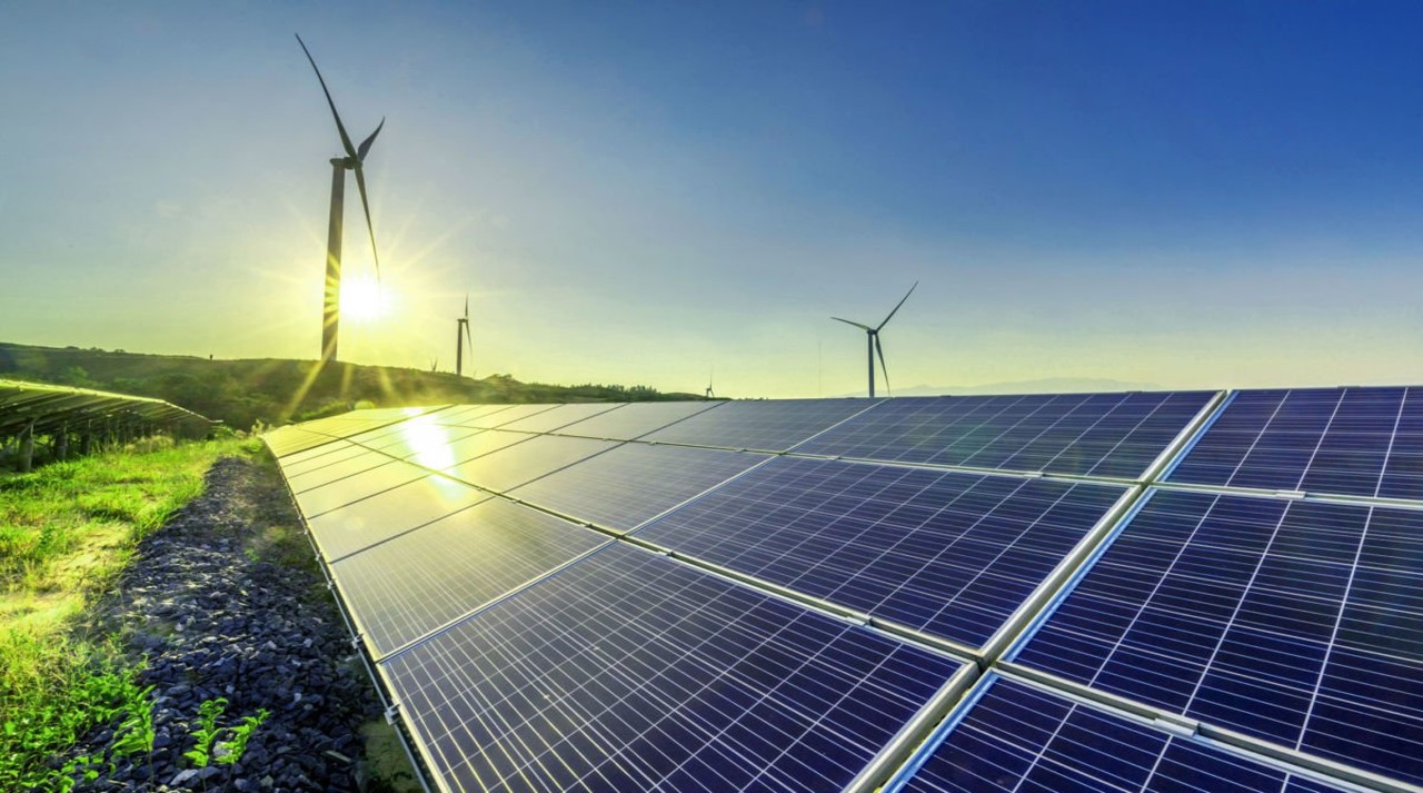 Vasudha - solar panels with wind turbines in the distance