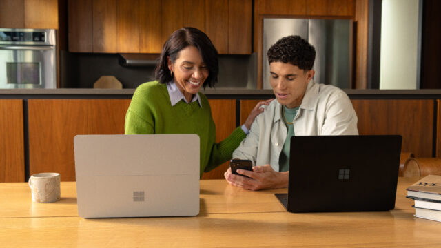 Two individuals with their laptop discussing at a kitchen table.