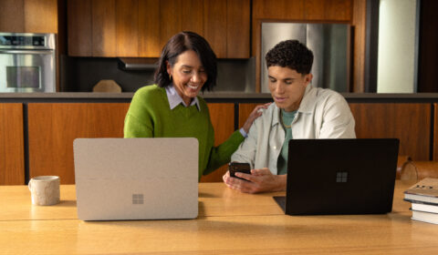 Image of two individuals and their laptops discussing by a kitchen table