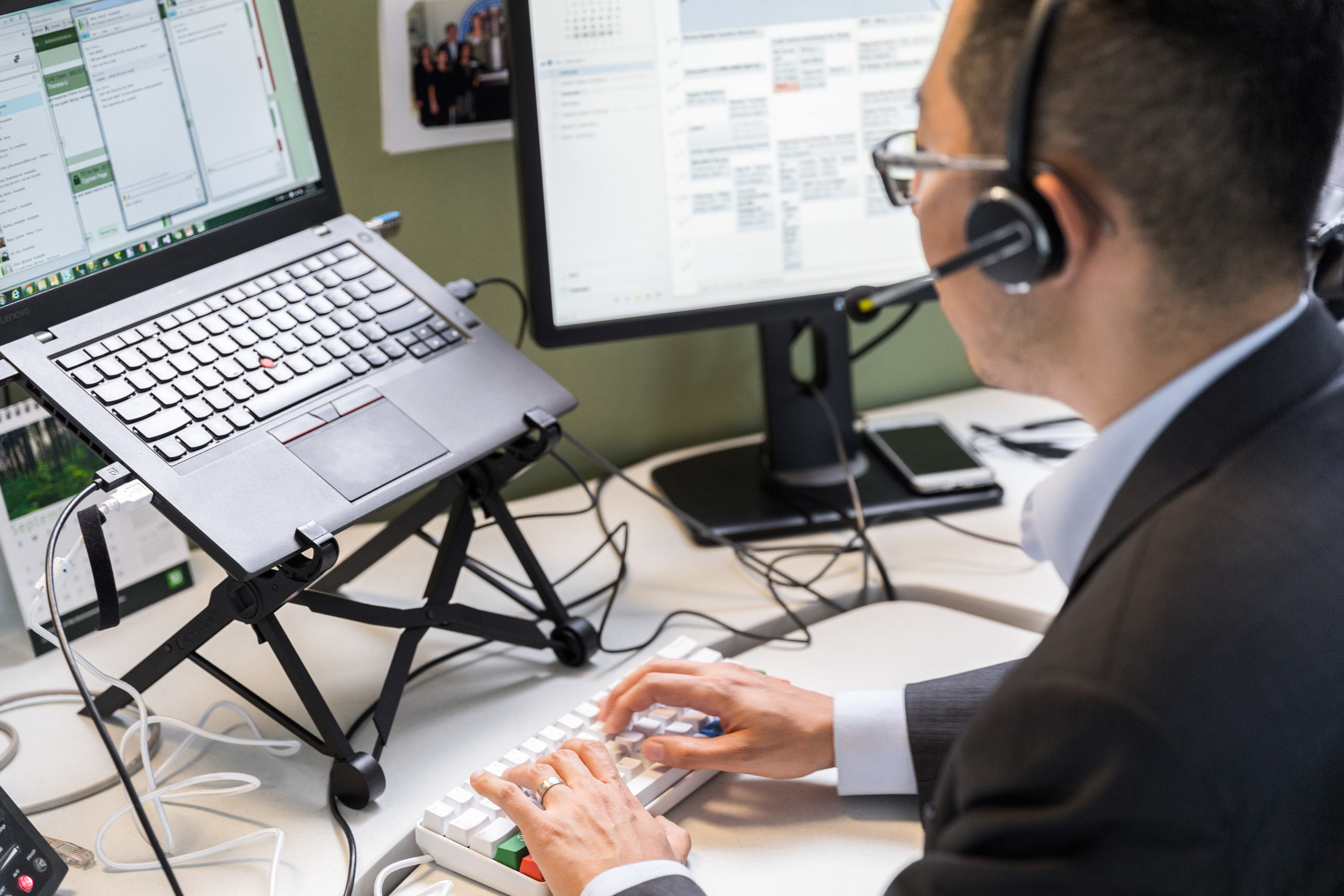 Male worker sitting at cubicle desk in financial office, wearing glasses and phone headset