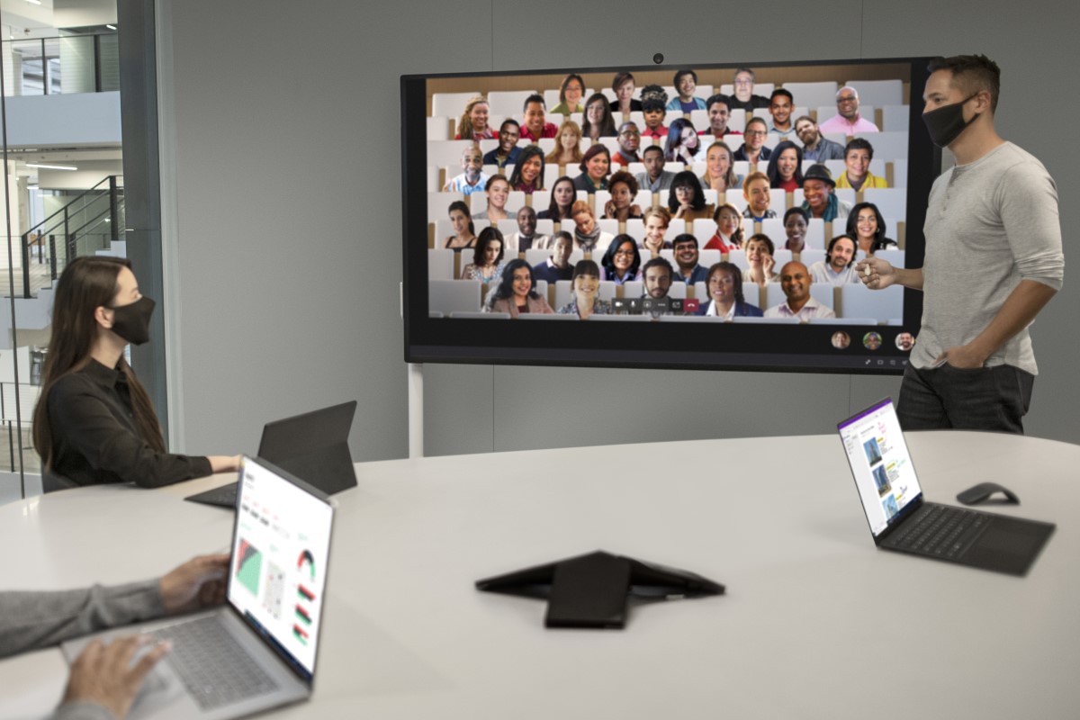 Two adults in masks collaborating while on a Microsoft Teams Together Mode meeting on a Surface Hub 2S 85&rdquo; device