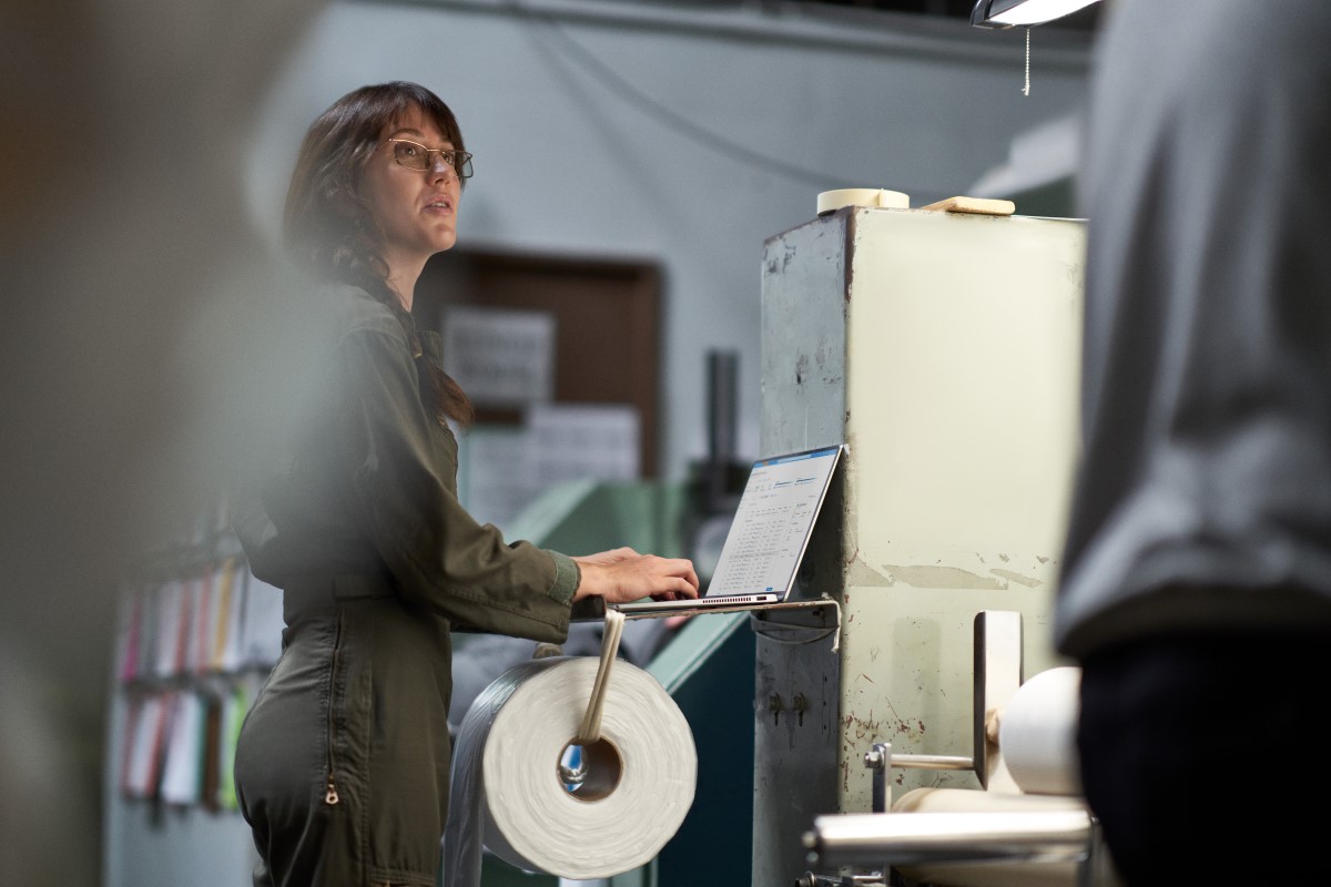 CEO of textile manufacturing plant working on shop floor analyzing data on her laptop