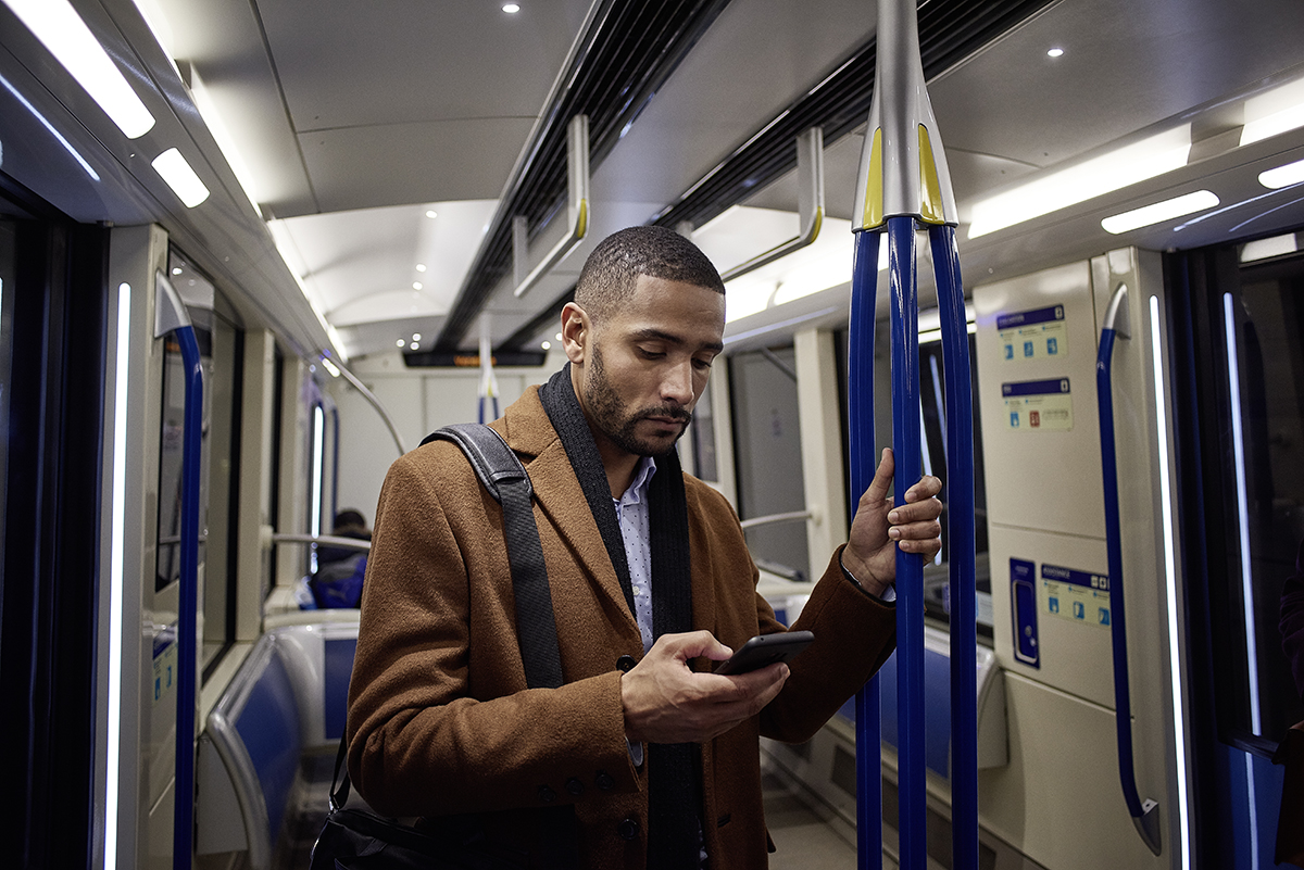 Male business professional standing on subway looking at smart phone mobile device