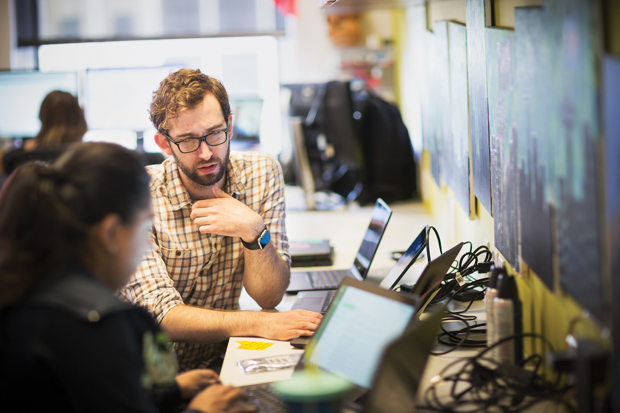 A man standing and looking at a colleague who is typing on a laptop