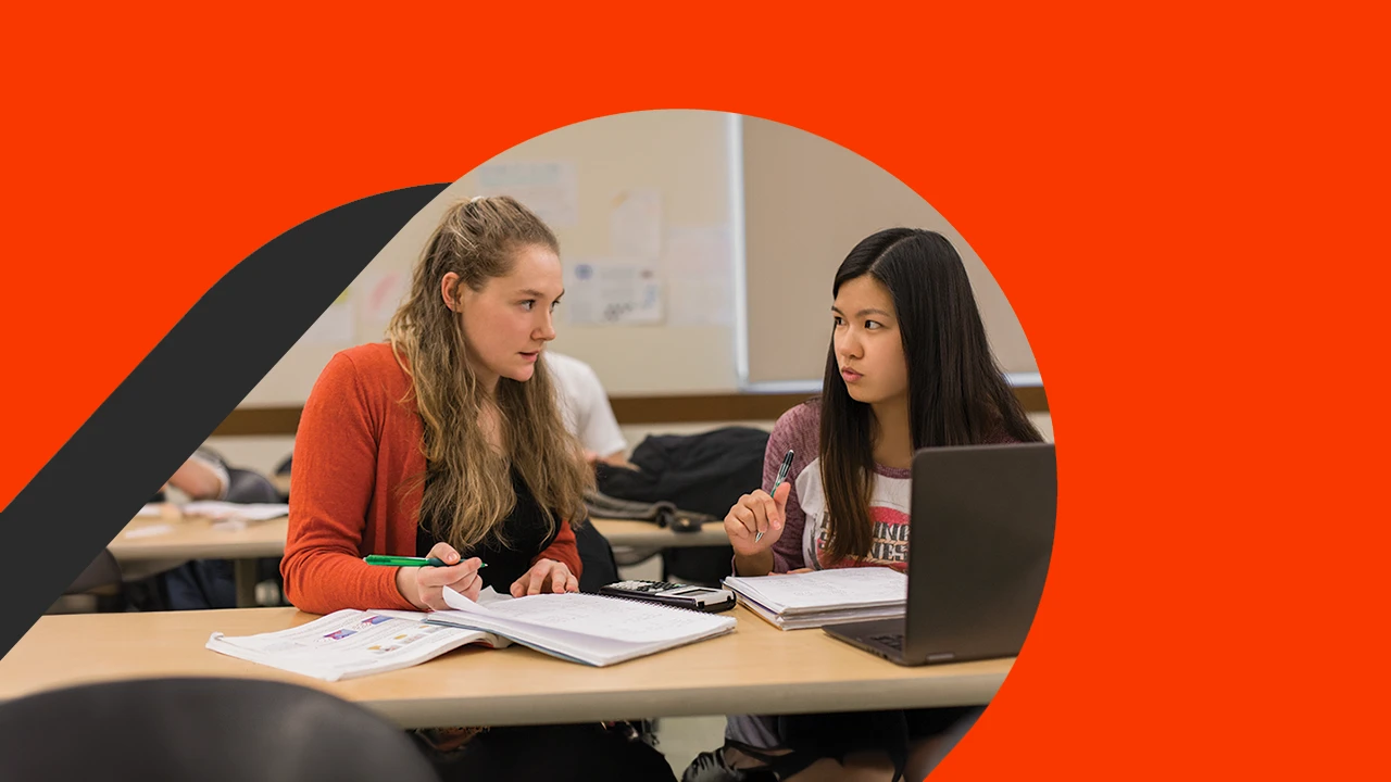 Two female students study together with open books and a device