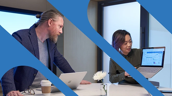 A woman and a man men working in a meeting room with Surface laptops. The woman is holding up her laptop and presenting her screen