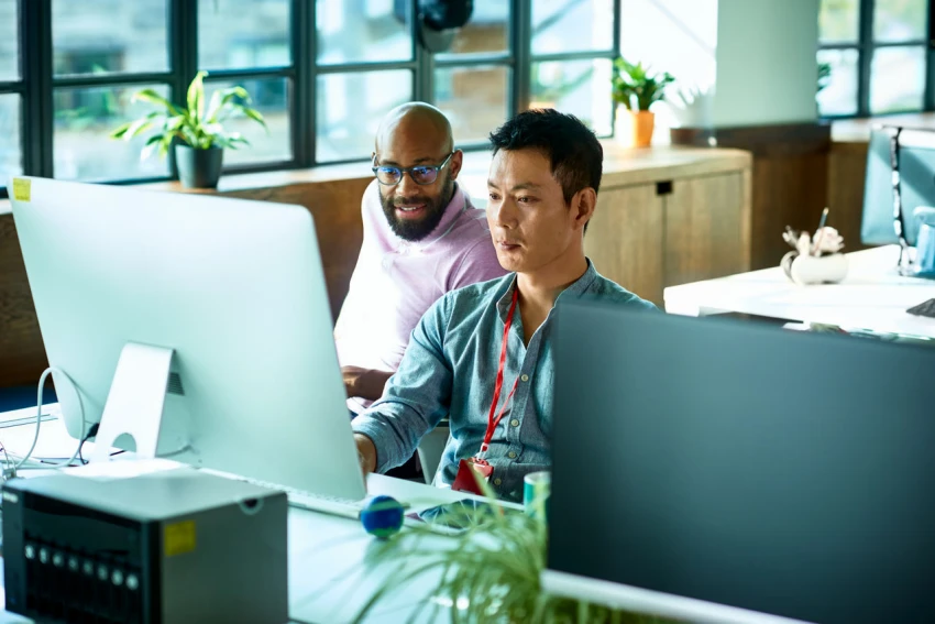 Two men look at a computer screen in a sunny office