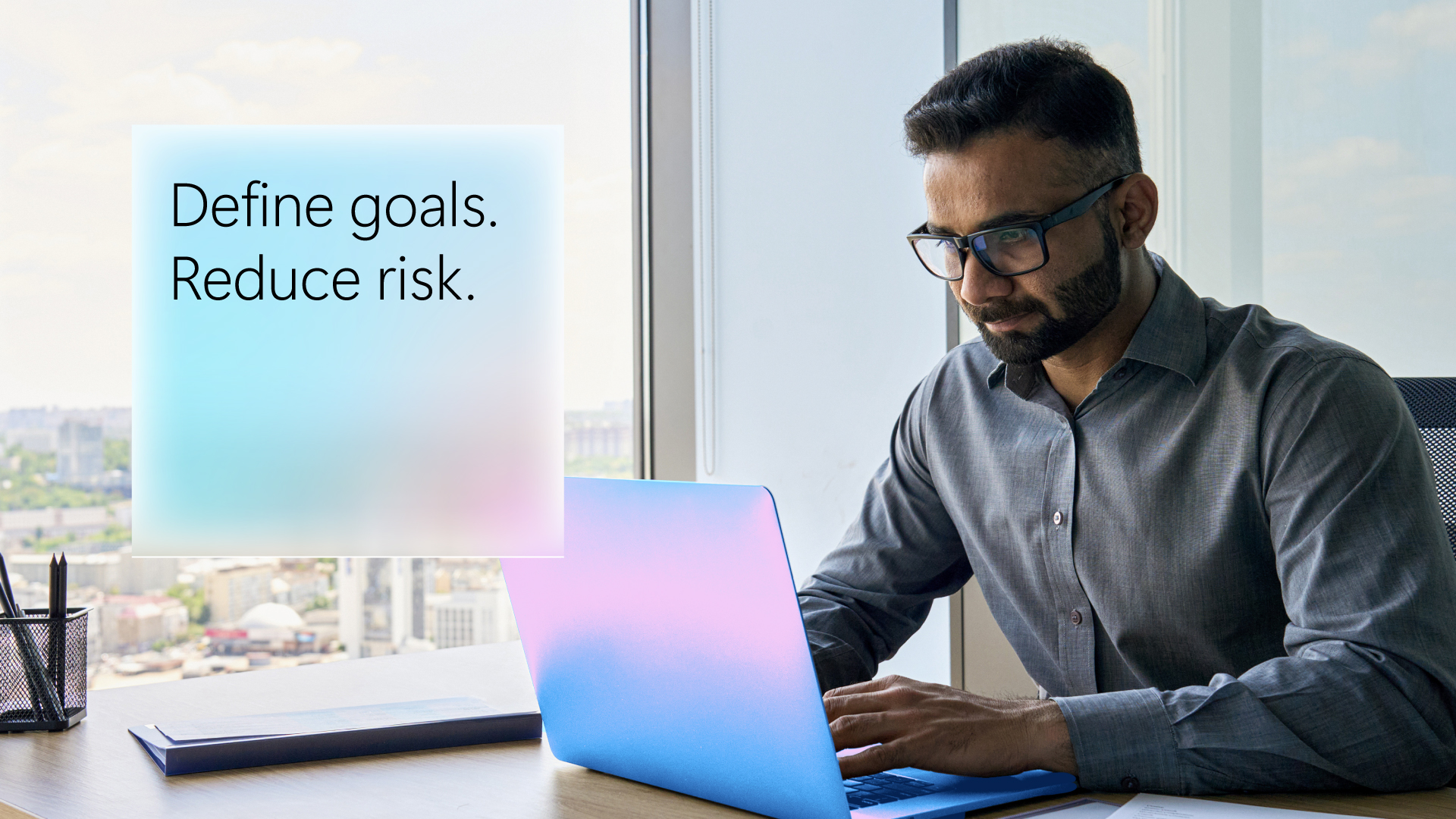 A man looks at a laptop screen. The words define goals, reduce risk are in the corner