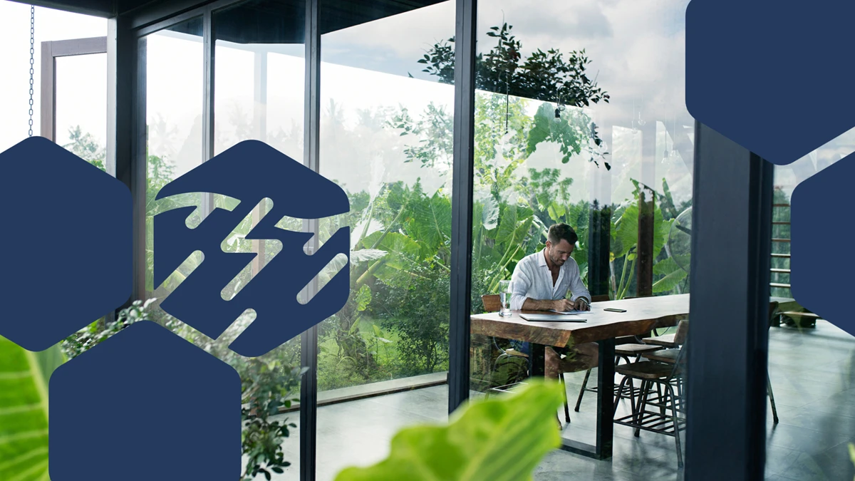 A man sitting at a table in front of a lush garden, writing