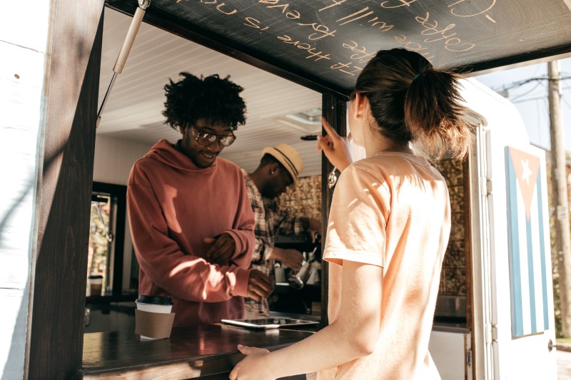 Propriet&aacute;rio de um food truck ajuda um cliente e anota um pedido de caf&eacute; usando um tablet digital